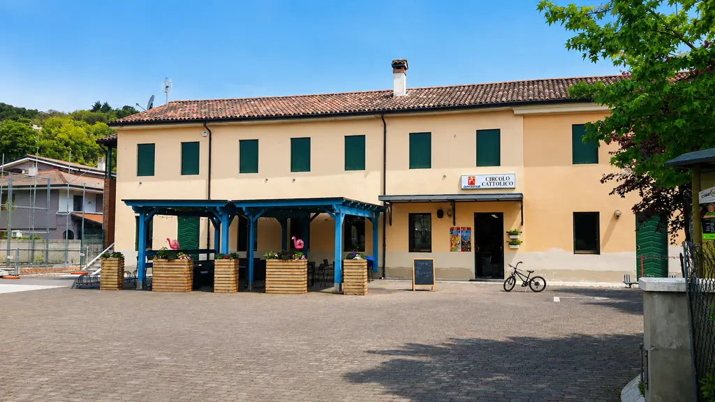 La facciata del Circolo Cattolico di Magrè con il portico blu e il cartello